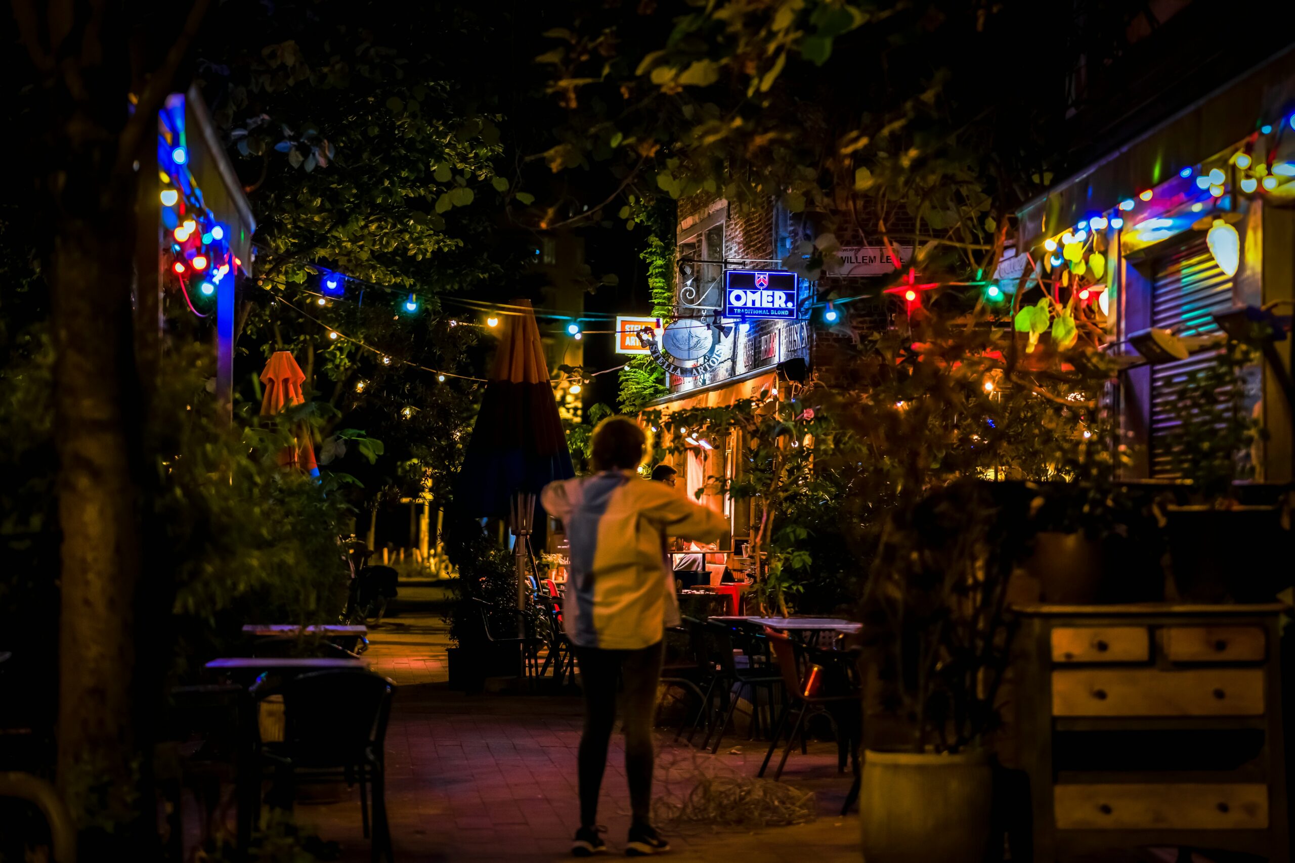 Person walking through a warmly lit outdoor bar area at night
