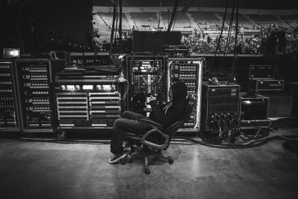 Backstage technician seated beside audio equipment before a live concert