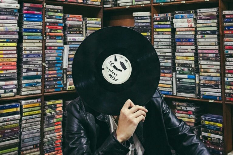 Person holding a vinyl record in front of shelves filled with music cassettes