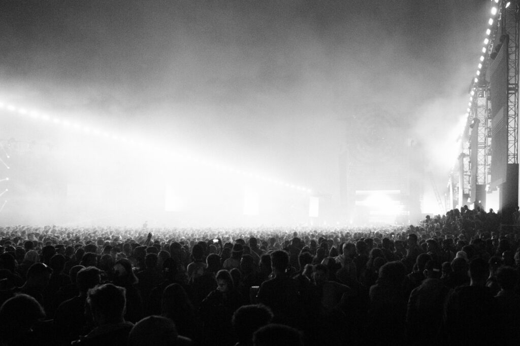 Large concert crowd in a dark venue facing a brightly lit stage